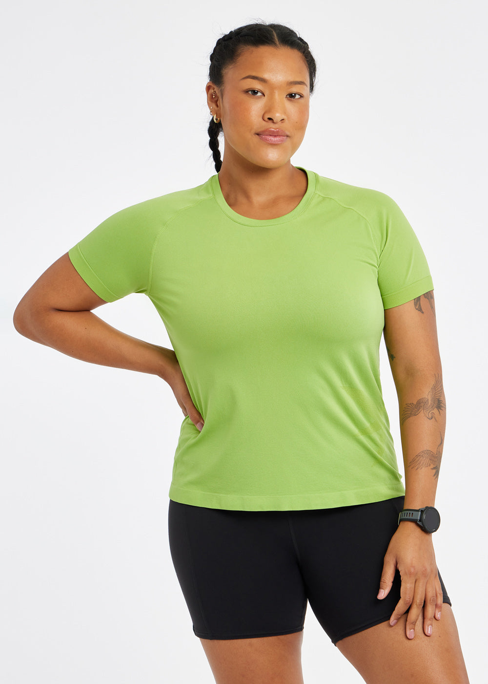 Woman wearing a green running short sleeve and black compression shorts, alternate front view